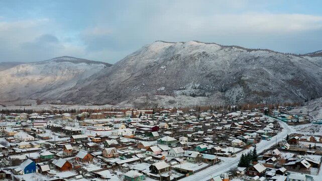 Aerial view of Aktash village nestled amid snow-covered mountains, a serene landscape of rooftops and frosted trees, Aktash, Altai Republic, Russia.