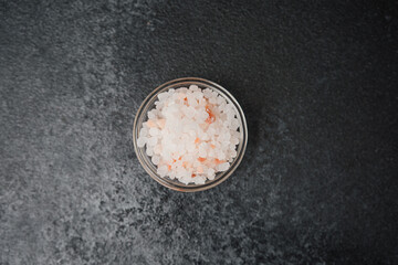 Glass bowl filled with pink himalayan salt on black stone background