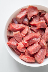 Raw meat in a white bowl on a white background. Red meat products. Finely chopped pieces of beef for cooking. Fresh ingredients for marinating and barbecue