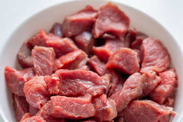 Raw meat in a white bowl on a white background. Red meat products. Finely chopped pieces of beef for cooking. Fresh ingredients for marinating and barbecue