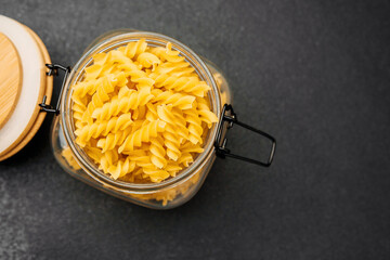 Freshly twirled pasta in a glass jar on a dark textured surface