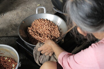 A grandmother is frying peanuts until they turn brown in a frying pan while sitting. The photo was...