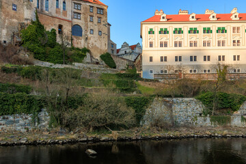 Fototapeta premium Historic czech buildings overlooking riverbank with lush greenery