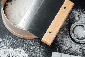 Kitchen tools for baking with flour and a bench scraper on a countertop