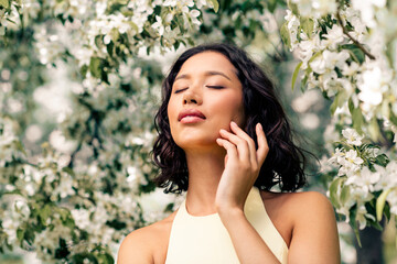 Gorgeous woman enjoying a sunny spring day amidst blooming trees, exuding beauty and elegance with...