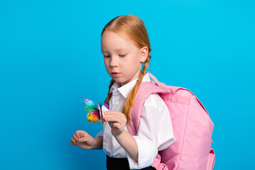 Adorable schoolgirl with red hair holding a butterfly, wearing a pink backpack, standing against a...
