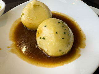 Two german potato dumplings with rich gravy and chives on white plate