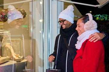 Happy couple admiring jewelry in a shop window during christmas season
