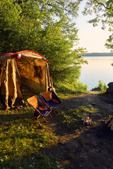 a tent with chairs and a burning campfire by the lake