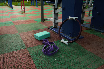 Gym equipment objects in outdoor urban street sport ground with safe rubber surface green red colors. Dumbbell, pilates ring, yoga block, fitness band lying on the floor with no people