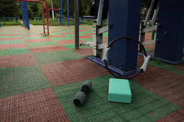 Gym equipment objects in outdoor urban street sport ground with safe rubber surface green red colors. Dumbbell, pilates ring, yoga block, fitness band lying on the floor with no people