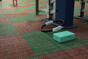 Gym equipment objects in outdoor urban street sport ground with safe rubber surface green red colors. Dumbbell, pilates ring, yoga block, fitness band lying on the floor with no people