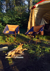 a tent with chairs and a burning campfire by the lake