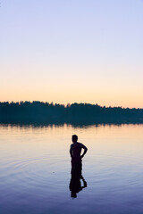 A man stands in a lake at sunset