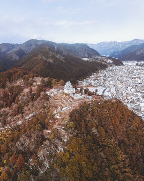 Aerial view of Gujo Hachiman Castle standing majestically atop a hill, contrasting with the snow-dusted town and the rugged, forested mountains beyond, Gujo Hachiman, Gifu, Japan.