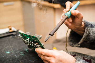 Man at home is soldering a circuit board with a soldering iron, smoke rises from electronic components.