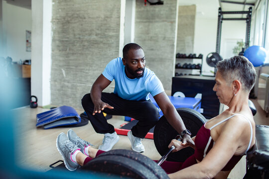 Personal trainer coaching senior woman on weightlifting exercise at the gym