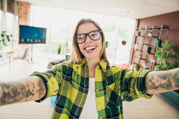 Bright and cheerful young woman in a stylish indoor office space taking a fun selfie, expressing...