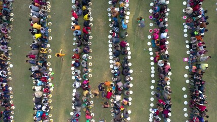 Bogura, Bangladesh - 25 July 2025: Aerial view of people seated in rows, enjoying a communal meal outdoors, with plates neatly aligned on green grass.
