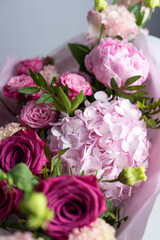 Pink bouquet of roses, peonies, eustoma and hydrangea on a light background. Festive professional flower arrangement in soft pink tissue paper. Romantic bouquet of buds and greenery close-up
