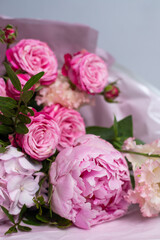 Pink bouquet of roses, peonies, eustoma and hydrangea on a light background. Festive professional flower arrangement in soft pink tissue paper. Romantic bouquet of buds and greenery close-up