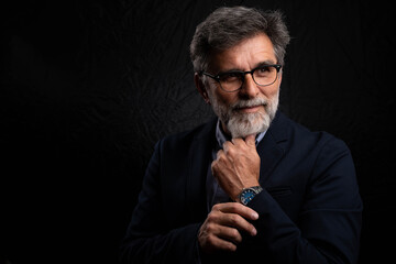 Portrait of confident middle-aged man posing in studio against dark background, stylish and serious mood

