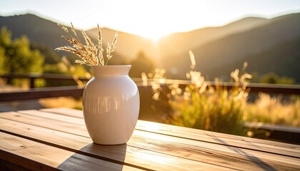 White Ceramic Vase with Dried Stems on Wooden Table Under Sunlight with Blurred Mountain Scenery