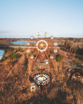 Aerial view of a desolate, rusting Ferris wheel and merry-go-round stand forlornly amid withered grasses, a haunting reminder of forgotten joy, &Aring;&OElig;saki, Miyagi, Japan.