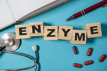 Wooden blocks spelling enzyme on a blue background with medical tools and capsules nearby