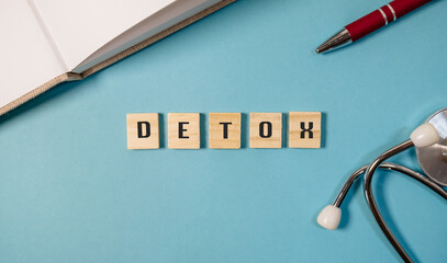 Detox concept with wooden letter tiles on a blue background alongside a pen and stethoscope