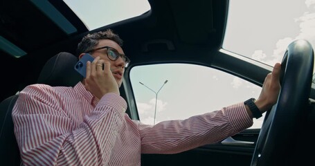 A man is talking on a mobile phone while driving a car. Close-up of his focused face