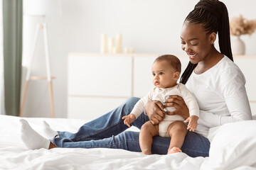 Childhcare And Babyhood. Portrait of adorable black infant in bodysuit sitting on mother's lap,...