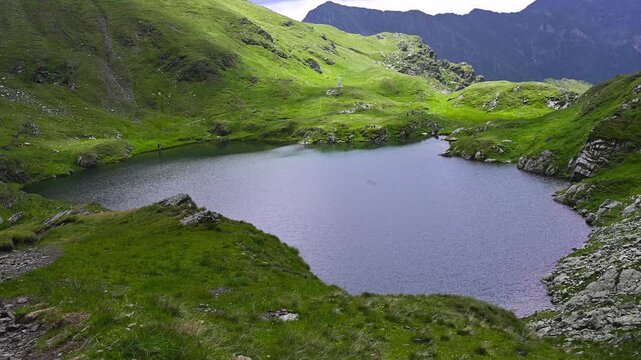Mountain lake surrounded by green hills and rocky slopes in the Fagaras Mountains, Romania. 
