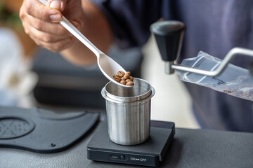 Person using digital scale to measure coffee beans in a stainless steel container du coffee brewing process in a modern kitchen setup