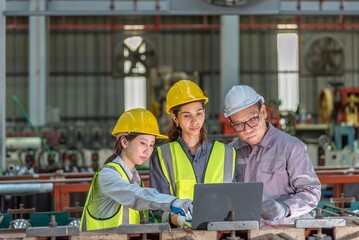 Group of three industrial workers wea safety helmets working together with a laptop in a manufactu...