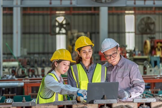 Group of three industrial workers wea safety helmets working together with a laptop in a manufactu or workshop environment, collaboration and safety concept