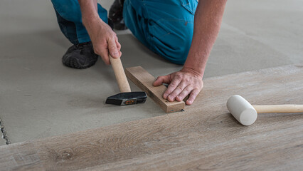 Floating floor work. The worker's hands taps the board of vinyl plank to lock the click system. He is using hammer and wooden plank.