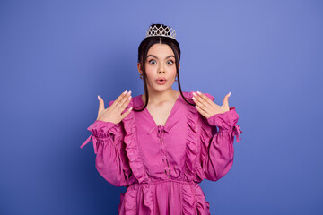 Glamorous woman in vibrant pink dress and tiara poses with expressive surprise against violet background © deagreez