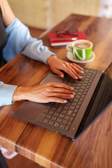Female professional typing on laptop with cappuccino nearby, wooden workspace reflecting remote work lifestyle