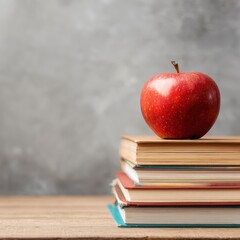Stack of aged books topped with a bright red apple set against a textured gray backdrop