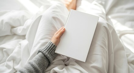 A person is holding a blank book while sitting in bed