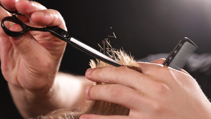 Young Man with Beard at Barber Shop. Barber is Preparing his Haircut. Dark Atmosphere, Black Background. Concept of Barber and a Client.