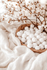 A wicker basket filled with white yarn balls is placed on a soft fabric surface beneath cotton branches. Cozy, soft texture, natural decor, minimalistic