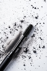 Mascara wand lies on a surface scattered with black particles. Makeup, beauty, cosmetics, elegance, texture