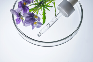 A drop of serum and a pipette with pansies in close-up.