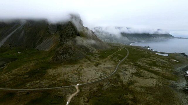 Aerial view of the rugged landscape with mountains shrouded in mist, contrasted by the calm waters and winding roads, Hvalnes, M&uacute;la&thorn;ing, Iceland.