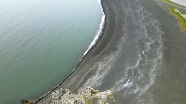 Aerial view of the stark contrast of the dark volcanic sand meeting the pale green sea at Hvalnes, the East Fjords, creating a mesmerizing scene, Hvalnes, M&uacute;la&thorn;ing, Iceland.