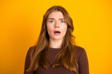 Surprised young woman with long brown hair against vibrant yellow background showcasing casual...