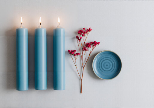 Three tall blue candles with warm flames, a shallow blue bowl, and dried lavender create a serene, minimalist ambiance. AI-generated.