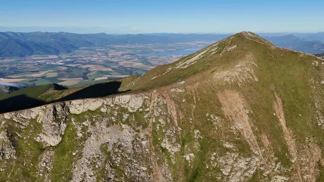 Aerial view of rolling mountainous terrain with lush green slopes casting deep shadows under a clear blue sky, ziar, zilina Region, Slovakia.